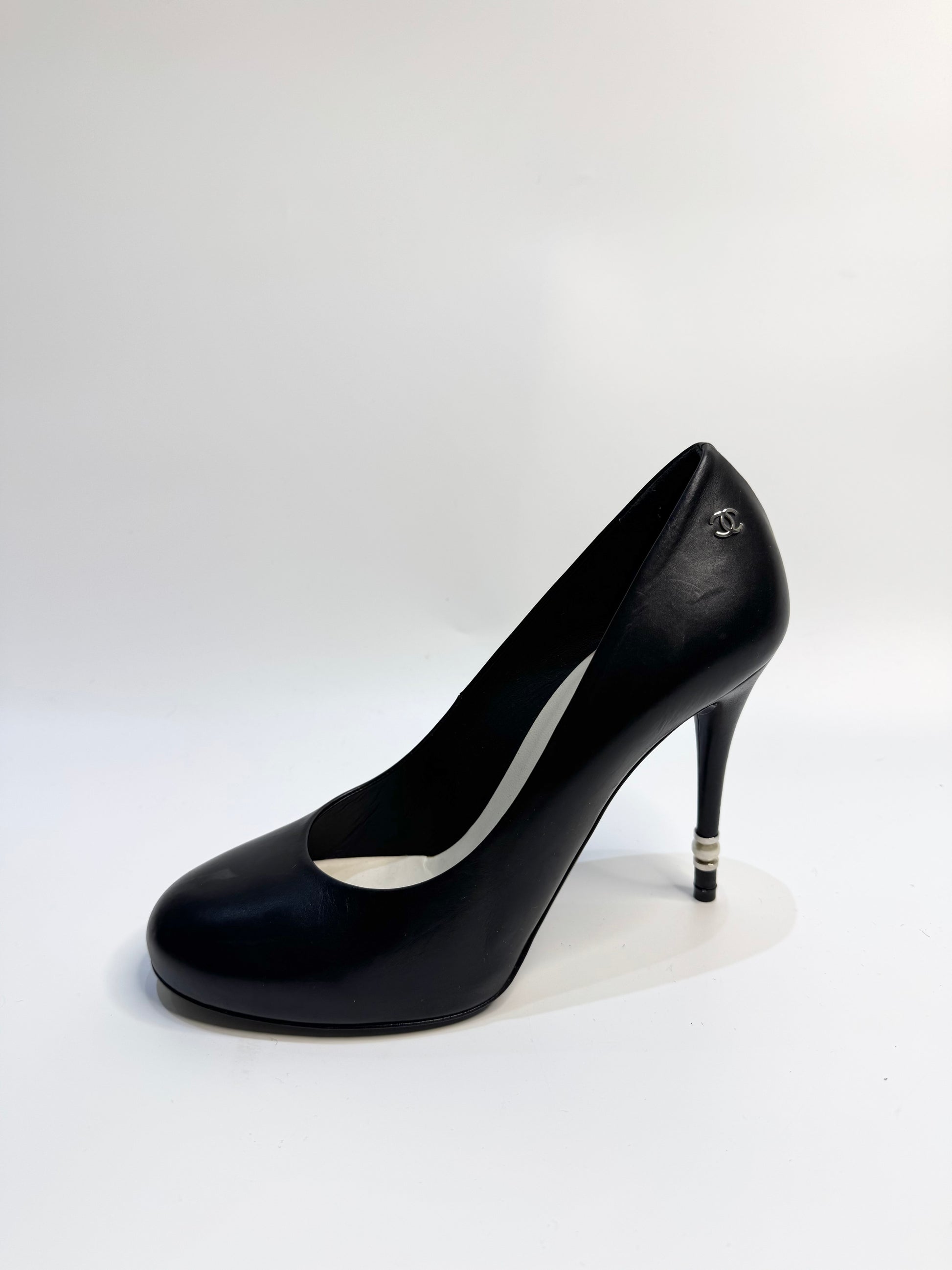 CHANEL black leather pumps with a pearl-embellished heel, highlighting the elegant curve and premium craftsmanship.