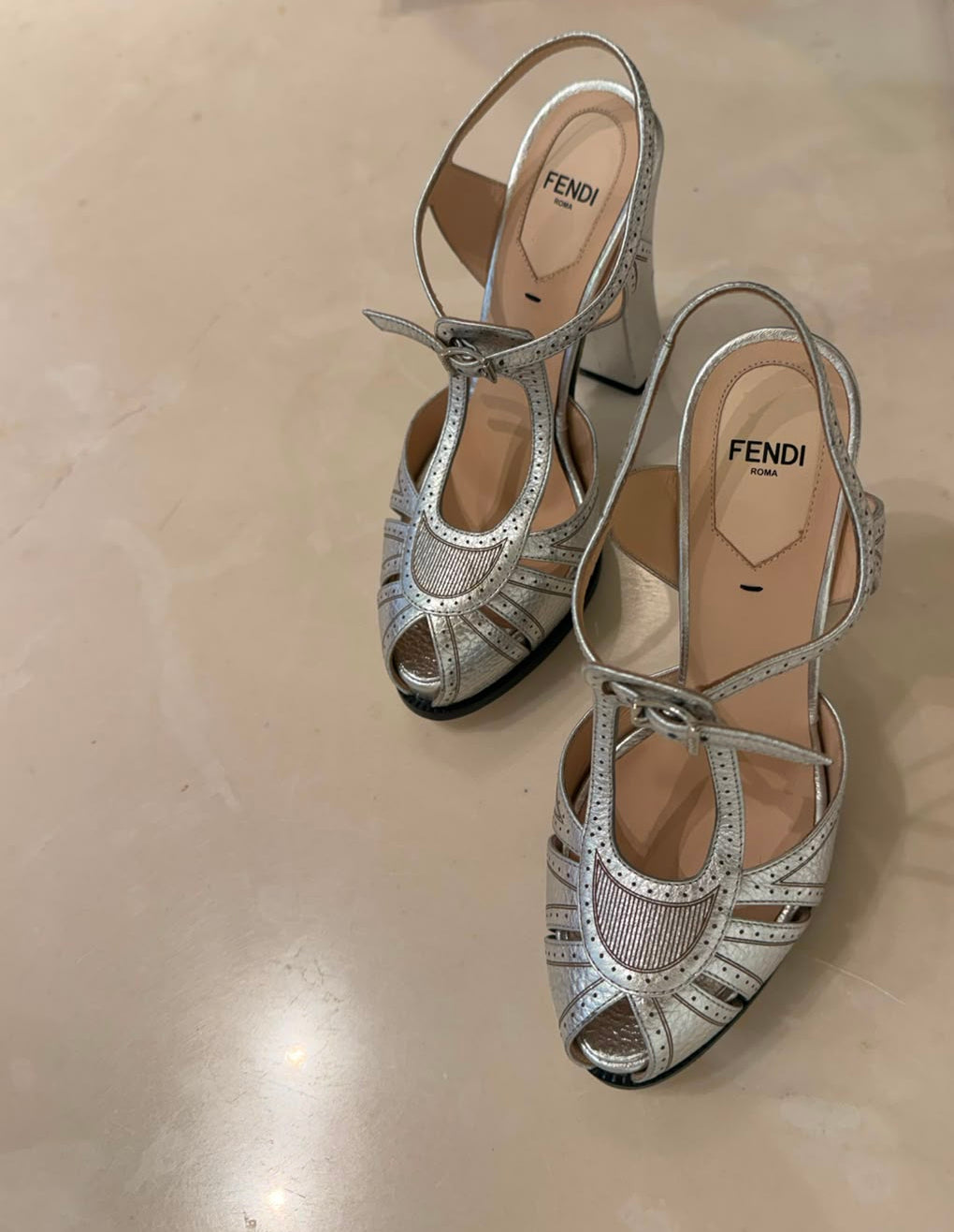 A pair of Fendi metallic silver strappy sandals with cutout details and ankle straps.