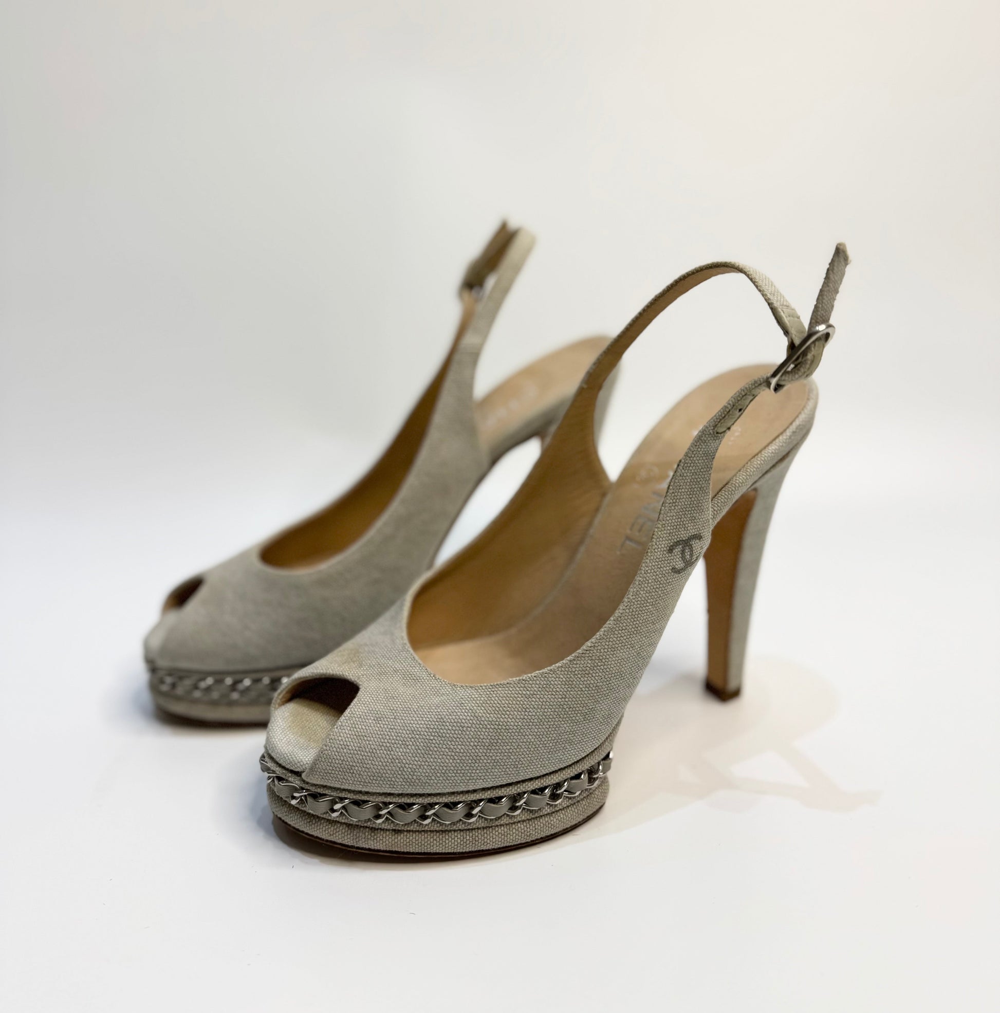 CHANEL Grey Canvas Peep Toe Sling Back Platform Sandals, size 38. The image highlights the side profile of the shoes, showcasing the platform heel, peep toe design, and adjustable sling back strap. The shoes are displayed on a reflective surface