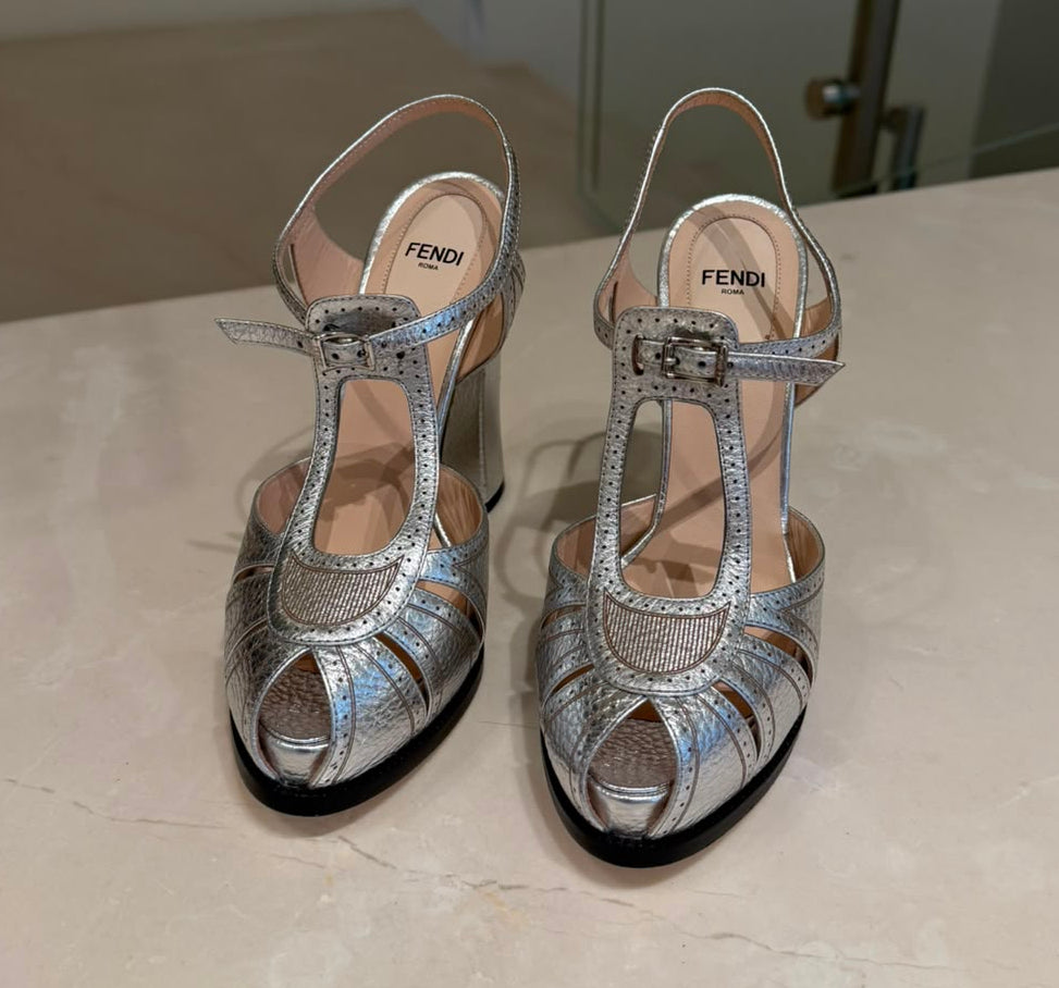 A pair of Fendi metallic silver peep-toe high heels with strappy T-strap details and rhinestone embellishments.