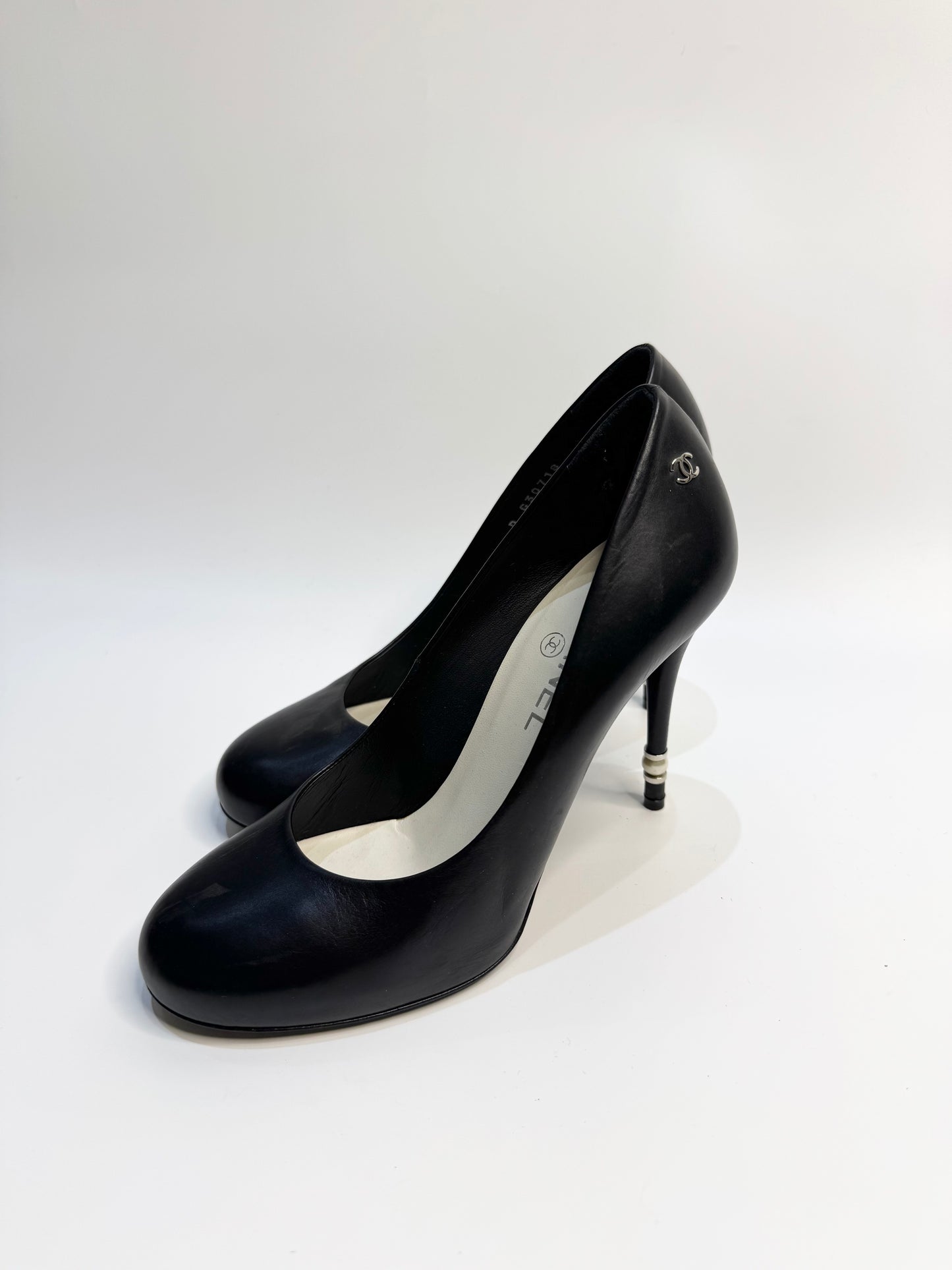 CHANEL black leather pumps with a pearl-embellished heel, highlighting the elegant curve and premium craftsmanship.