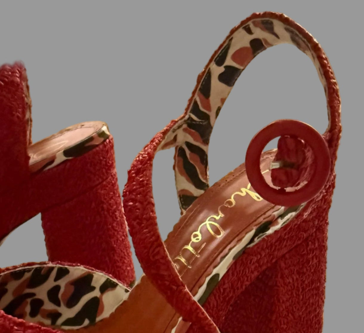 Red high-heeled shoes with leopard print interior on a light surface.