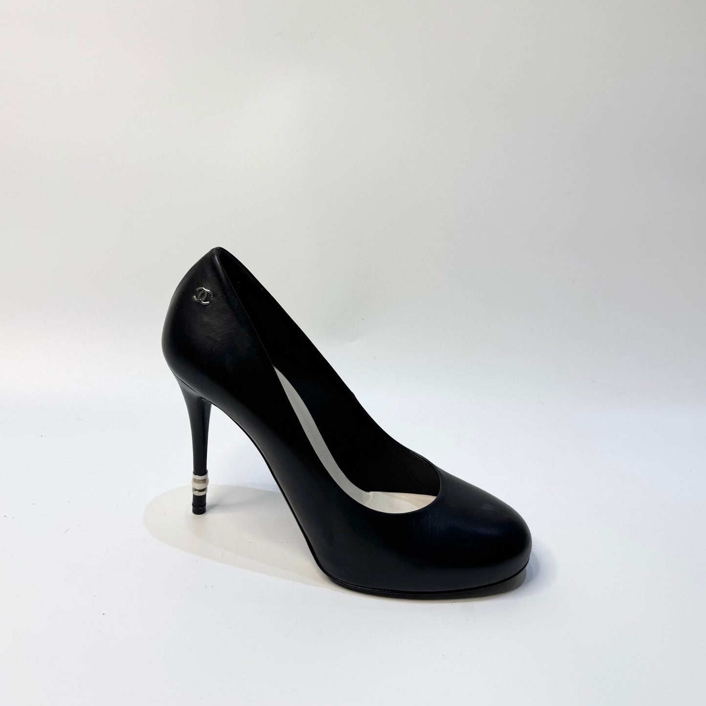 CHANEL black leather pumps with a pearl-embellished heel, highlighting the elegant curve and premium craftsmanship.