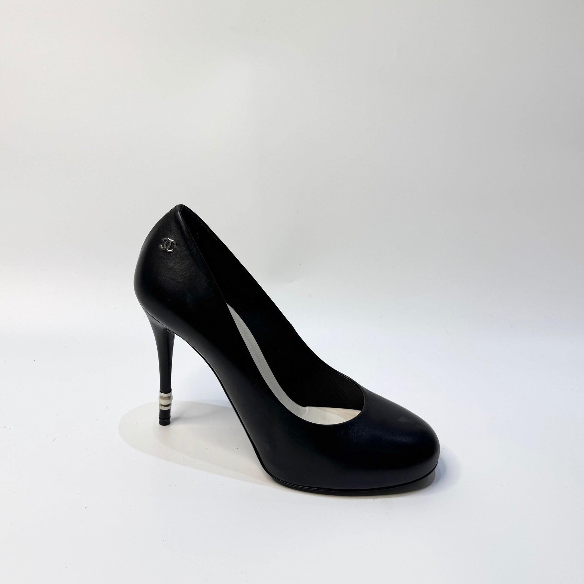 CHANEL black leather pumps with a pearl-embellished heel, highlighting the elegant curve and premium craftsmanship.