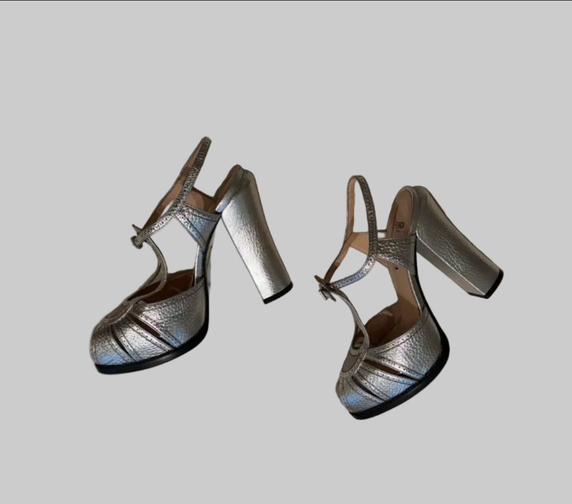 A pair of metallic silver high-heeled sandals with block heels and ankle straps.