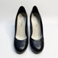 A pair of CHANEL black leather pumps displayed from the front, showcasing their sleek, pointed-toe design.