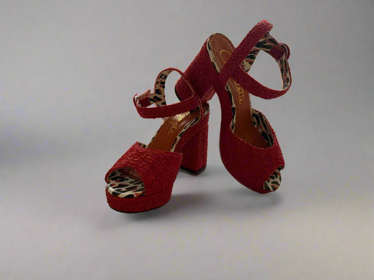 Red high-heeled shoes with leopard print accents on a reflective surface.