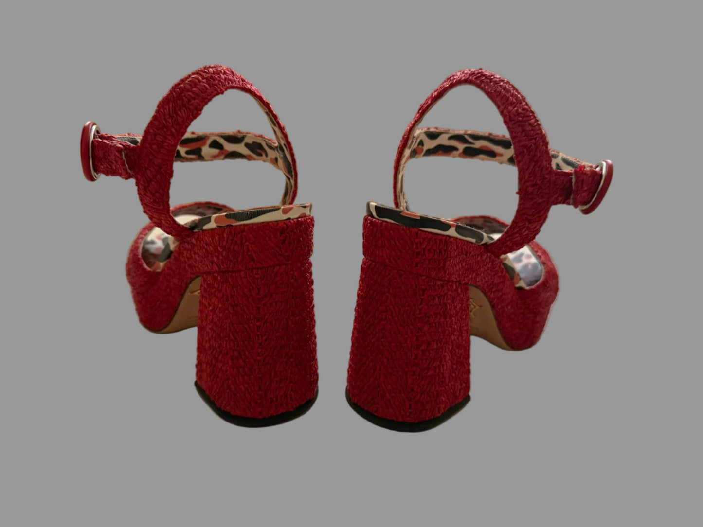 Pair of red high-heeled shoes on a light surface with a mirror reflection.