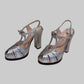 A pair of metallic silver high-heeled sandals with T-strap details and block heels.