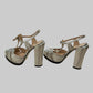 A pair of women's metallic silver high-heeled sandals with ankle straps and rhinestone trim.