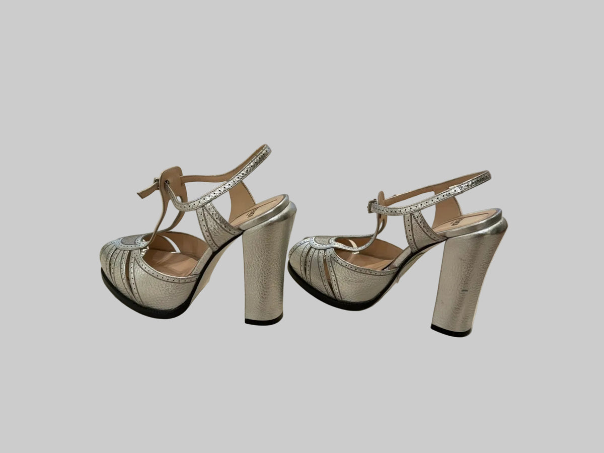 A pair of women's metallic silver high-heeled sandals with ankle straps and rhinestone trim.