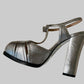 A pair of metallic silver high-heeled sandals with a block heel and strappy design.
